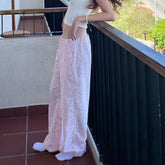 Person wearing a white top and light pink pants on a balcony.